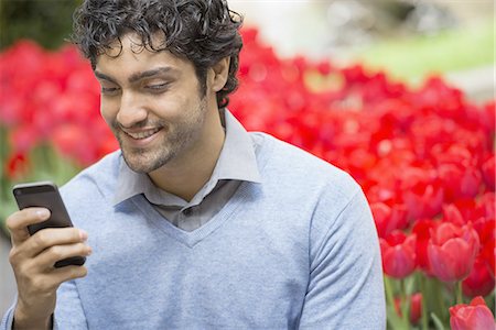 simsearch:6118-07354515,k - Urban Lifestyle. A man in the park, using his mobile phone. A bed of red flowering tulips in the background. Stock Photo - Premium Royalty-Free, Code: 6118-07440879