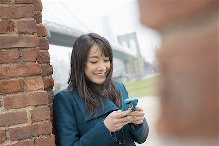 simsearch:693-05552824,k - New York city. The Brooklyn Bridge crossing over the East River. A woman leaning against a brick wall, checking her phone. Stock Photo - Premium Royalty-Free, Code: 6118-07440941