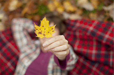 fall season people - A woman lying on a red tartan picnic blanket, looking upwards, holding a maple leaf. Stock Photo - Premium Royalty-Free, Code: 6118-07439807