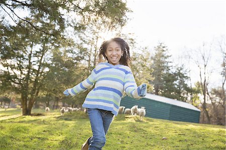simsearch:6118-07354445,k - A young girl in a  blue stripy top running in a field of sheep at an animal sanctuary. Stock Photo - Premium Royalty-Free, Code: 6118-07439823