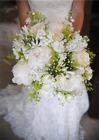 A woman in a white dress, a bride holding a bridal bouquet of white flowers, large white roses and peonies, with delicate yellow flowers and green leaves. Stock Photo - Premium Royalty-Free, Code: 6118-07521750