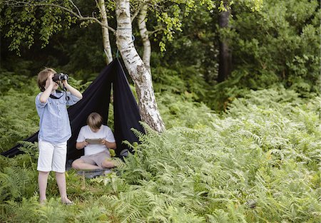 Two boys camping in New Forest. One sitting under a black canvas shelter.  One boy looking through binoculars. Stock Photo - Premium Royalty-Free, Code: 6118-07521781