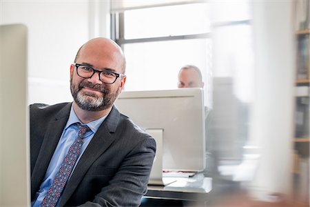 pictures of bald men in glasses - Office life. A man in a suit and tie sitting at his desk looking around his computer. Stock Photo - Premium Royalty-Free, Code: 6118-07781698
