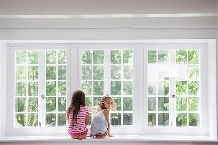 Two girls sitting side by side by a large window. Stock Photo - Premium Royalty-Free, Code: 6118-07781844