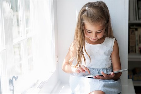 A young girl sitting at a window seat, using a digital tablet. Stock Photo - Premium Royalty-Free, Code: 6118-07781848