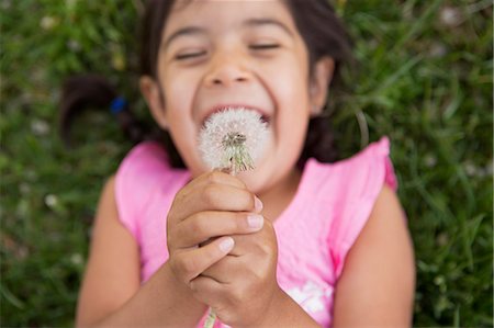 A girl lying on the ground, holding a dandelion seedhead clock. Stock Photo - Premium Royalty-Free, Code: 6118-07732061