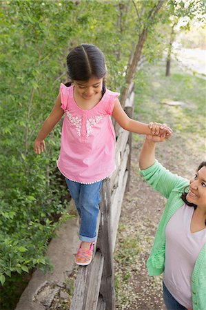 A young girl in a pink shirt and jeans, walking along a fence holding her mother's hand. Stock Photo - Premium Royalty-Free, Code: 6118-07732069