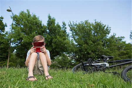 simsearch:649-03775589,k - A young boy sitting on the grass playing a hand held electronic game. Stock Photo - Premium Royalty-Free, Code: 6118-07732007