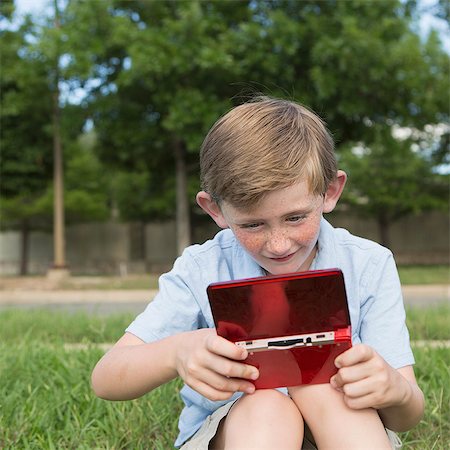simsearch:649-03775589,k - A young boy sitting on the grass playing a hand held electronic game. Stock Photo - Premium Royalty-Free, Code: 6118-07732008