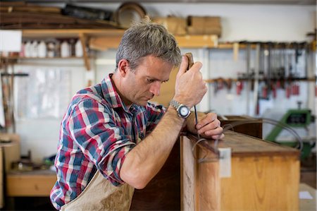 An antique furniture restorer using a handheld work tool and working on the polished top of a piece of furniture. Photographie de stock - Premium Libres de Droits, Code: 6118-08088595