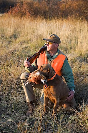 person full body shot crouching - A bird hunter and his trained dog with a dead pheasant in its mouth. Retriever. Stock Photo - Premium Royalty-Free, Code: 6118-08001529