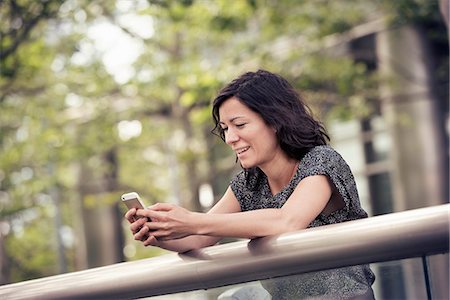 simsearch:6118-08243810,k - A woman leaning on a rail in a city park checking her cell phone Stock Photo - Premium Royalty-Free, Code: 6118-08243847