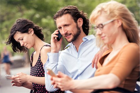 simsearch:6118-08243810,k - A man and two women seated on a bench in a park, checking their phones, one making a call. Stock Photo - Premium Royalty-Free, Code: 6118-08243862