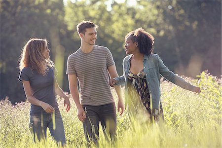 Three people, a man and two women walking through tall grass in a meadow. Stock Photo - Premium Royalty-Free, Code: 6118-08243896