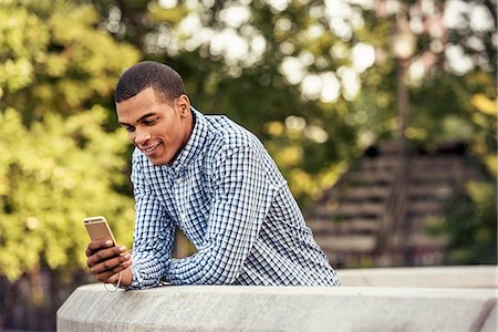 A man leaning on a parapet looking at a smart phone Photographie de stock - Premium Libres de Droits, Code: 6118-08243806