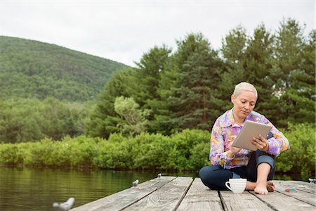 simsearch:6118-07122740,k - A woman sitting outdoors on a jetty using a digital tablet. Photographie de stock - Premium Libres de Droits, Code: 6118-08243922