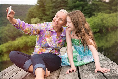 A woman and a child seated on a lake dock taking a selfie with a smart phone. Stock Photo - Premium Royalty-Free, Code: 6118-08243932