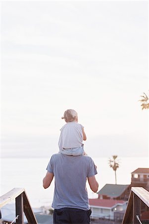 Rear view of a man carrying his young daughter on his shoulders. Stock Photo - Premium Royalty-Free, Code: 6118-08202497