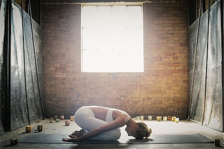 simsearch:6102-08942215,k - A blonde woman kneeling on a mat on the floor, stretching in a yoga pose, surrounded by lit candles. Stock Photo - Premium Royalty-Free, Code: 6118-08202433