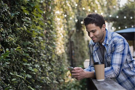 simsearch:6118-08243810,k - A man sitting at a cafe table outdoors, using his phone. Stock Photo - Premium Royalty-Free, Code: 6118-08394077