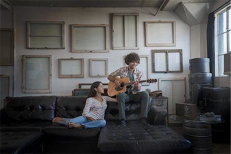 Loft decor. A wall hung with pictures in frames, reversed to show the backs. A man playing a guitar and a woman sitting on a sofa. Stock Photo - Premium Royalty-Free, Code: 6118-08394016