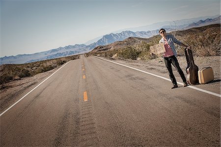 future of the desert - A man standing by the roadside, a hitchhiker with guitar and case, holding a sign saying Vegas or Bust. Stock Photo - Premium Royalty-Free, Code: 6118-08394223