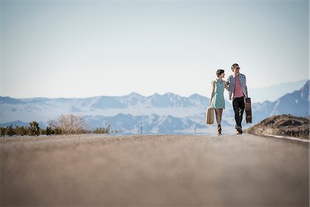 future of the desert - A young couple, man and woman, on a tarmac road in the desert carrying cases. Stock Photo - Premium Royalty-Free, Code: 6118-08394228