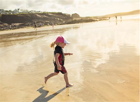 A child in a wetsuit and sunhat running on sand Stock Photo - Premium Royalty-Free, Code: 6118-08399563