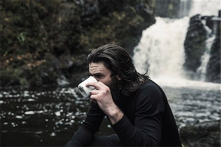 Wild camping. A man drinking from a cup by a fast flowing stream. Foto de stock - Sin royalties Premium, Código: 6118-08399661