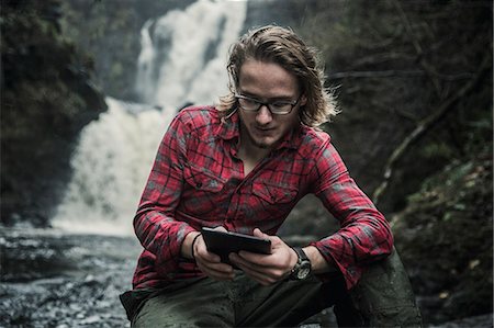 A man sitting by a fast flowing stream using a digital tablet. Foto de stock - Sin royalties Premium, Código: 6118-08399668