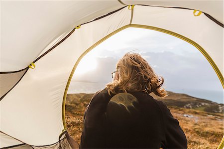 simsearch:6118-08399701,k - A man sitting in the shelter of a tent looking out. Stock Photo - Premium Royalty-Free, Code: 6118-08399684