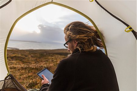 simsearch:6118-08399715,k - A man sitting in the shelter of a tent looking out, holding a digital tablet Stock Photo - Premium Royalty-Free, Code: 6118-08399686