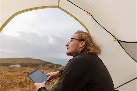 simsearch:6118-08399701,k - A man sitting in the shelter of a tent looking out, holding a digital tablet. Stock Photo - Premium Royalty-Free, Code: 6118-08399689