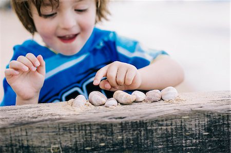 discovery - A boy at the beach counting shells lined up on a breakwater. Stock Photo - Premium Royalty-Free, Code: 6118-08313800