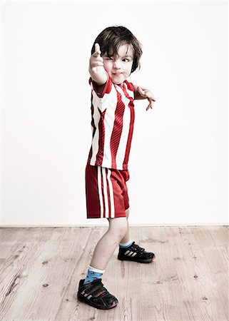 floor - A boy in red and white striped shirt and football shorts standing pointing at the camera. Stock Photo - Premium Royalty-Free, Code: 6118-08313801