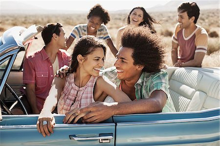 A group of friends in a pale blue convertible on the open road, driving across a dry flat plain surrounded by mountains. Photographie de stock - Premium Libres de Droits, Code: 6118-08488140