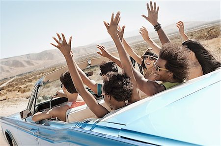 A group of friends in a pale blue convertible on the open road, driving across a dry flat plain surrounded by mountains. Photographie de stock - Premium Libres de Droits, Code: 6118-08488174