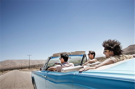 Three young people in a pale blue convertible car, driving on the open road across a flat dry plain, Photographie de stock - Premium Libres de Droits, Code: 6118-08488194