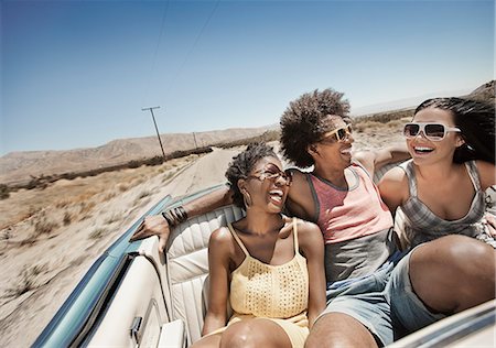 Three young people in a pale blue convertible car, driving on the open road across a flat dry plain, Photographie de stock - Premium Libres de Droits, Code: 6118-08488196