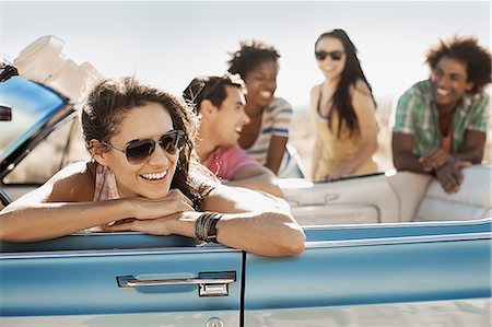 A group of friends in a pale blue convertible on the open road, driving across a dry flat plain surrounded by mountains. Stock Photo - Premium Royalty-Free, Code: 6118-08488139