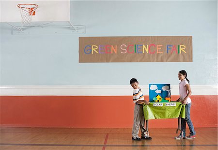 symbol for students education - A boy and girl carrying a table with a presentation on solar power, at a Green Science Fair event. Stock Photo - Premium Royalty-Free, Code: 6118-08488222