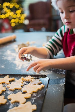 A boy in a Santa hat making Christmas biscuits, cutting out shapes. Stock Photo - Premium Royalty-Free, Code: 6118-08488468