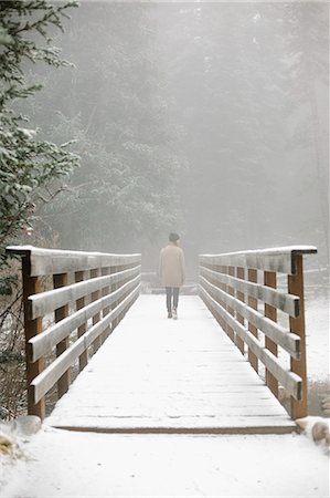 A woman walking on a footbridge in the mountains in snow. Stock Photo - Premium Royalty-Free, Code: 6118-08521818