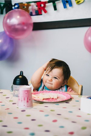 A child, a one year old girl at her birthday party, sitting in a high chair at a table. Stock Photo - Premium Royalty-Free, Code: 6118-08659995