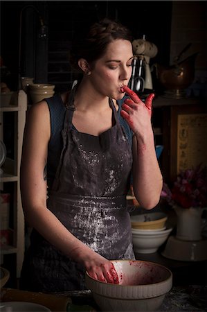 eat standing - Valentine's Day baking, young woman standing in a kitchen, preparing raspberry jam, licking her finger, tasting. Stock Photo - Premium Royalty-Free, Code: 6118-08660121