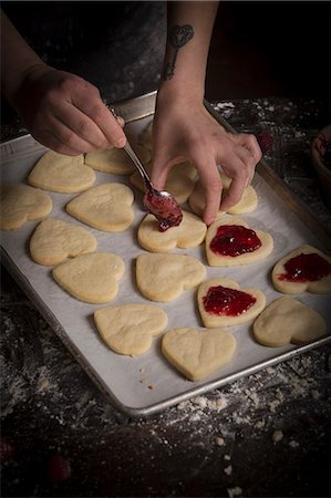 Valentine's Day baking, woman spreading raspberry jam on heart shaped biscuits. Stock Photo - Premium Royalty-Free, Code: 6118-08660133