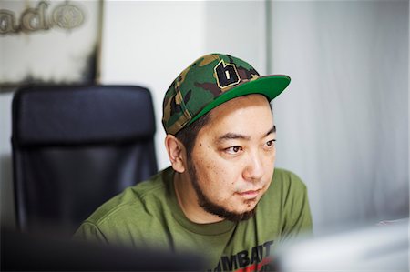 small business asian - Design Studio. A man wearing a baseball cap looking at a screen. Stock Photo - Premium Royalty-Free, Code: 6118-08762178