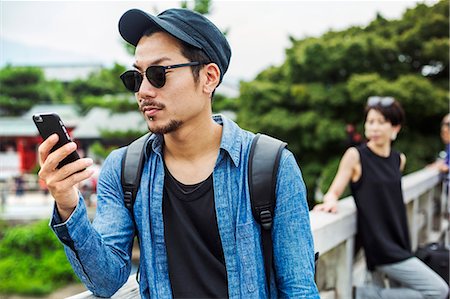 east asian (people) - A man looking at his smart phone, a woman behind him. Stock Photo - Premium Royalty-Free, Code: 6118-08762181