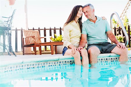 A couple seated side by side on the edge of a swimming pool. Stock Photo - Premium Royalty-Free, Code: 6118-08725780