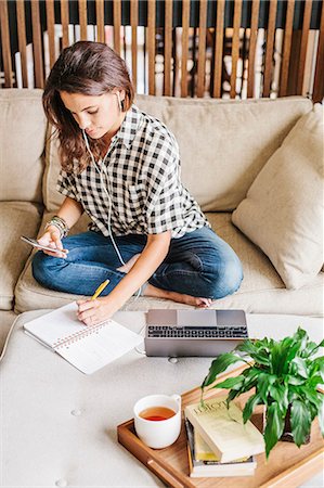 Woman with long brown hair sitting on a sofa with a laptop computer and notebook, working. Stock Photo - Premium Royalty-Free, Code: 6118-08729159